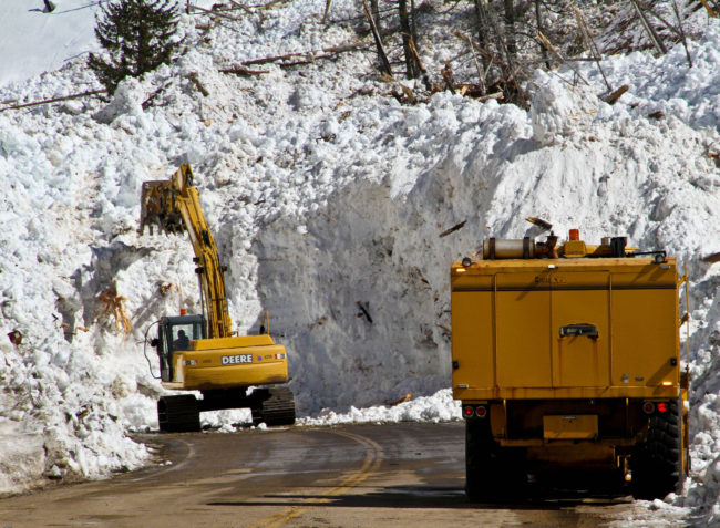 Avalanche cleanup crew clearing a highway road with heavy machinery.
