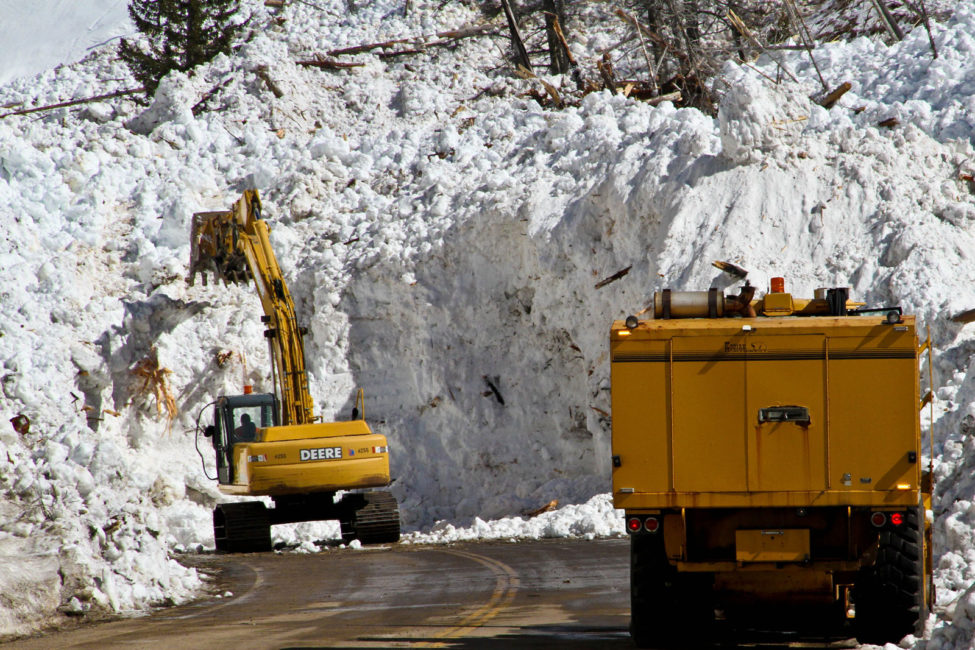 Avalanche cleanup crew clearing a highway road with heavy machinery.
